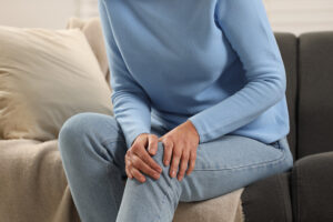 Mature woman suffering from knee pain on sofa indoors, closeup.