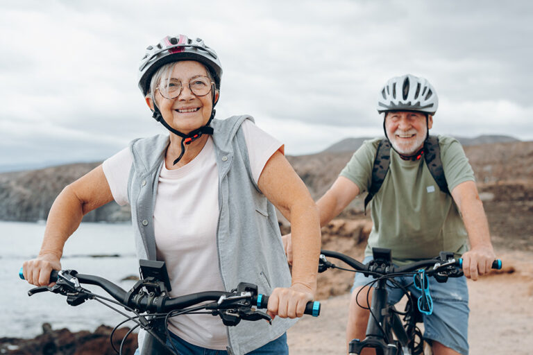 Senior couple riding bikes together in rocky beach enjoying outdoor.